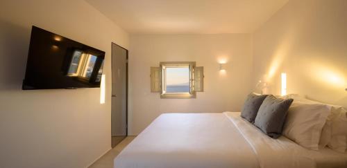 a bedroom with a large white bed and a television at Oia Treasures Art Suites in Oia