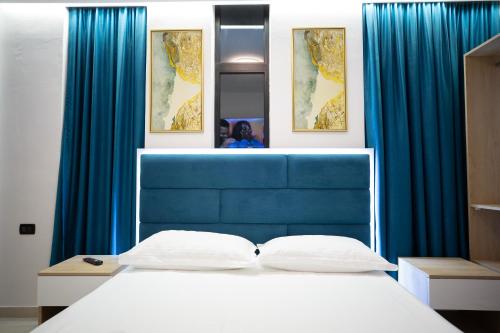 a bed with a blue headboard and blue curtains at Frekel Hotel in Tirana