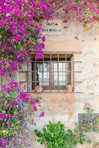 a window on a stone building with purple flowers at Casa rural con jacuzzi en centro histórico de Pals in Pals