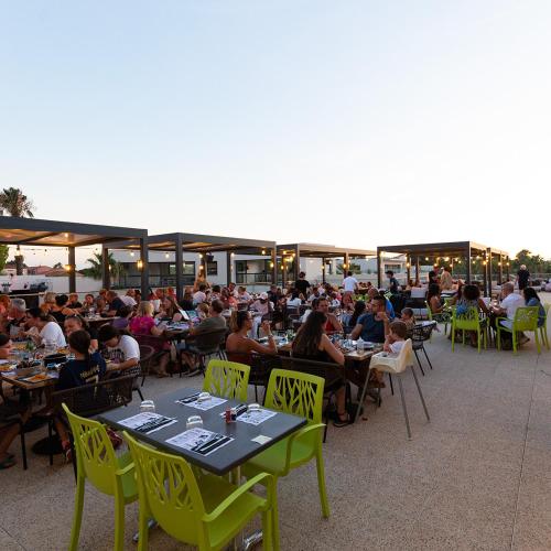 un grand groupe de personnes assises à des tables sur une terrasse dans l'établissement Mobil Home XXL 4 chambres - Camping Les Tropiques, à Torreilles