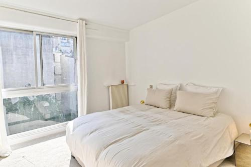 une chambre blanche avec un lit et une grande fenêtre dans l'établissement Appartement Spacieux avec Balcon Le Bon marché, à Paris