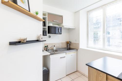 une cuisine avec des armoires blanches, un évier et une fenêtre dans l'établissement *Le Gicquel* T1 proche centre, à Brest