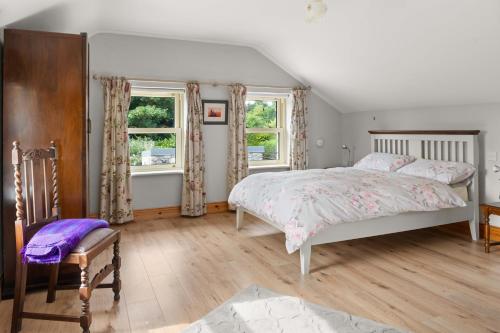 a bedroom with a bed and a chair and two windows at Joe's Corner House in Shanagarry
