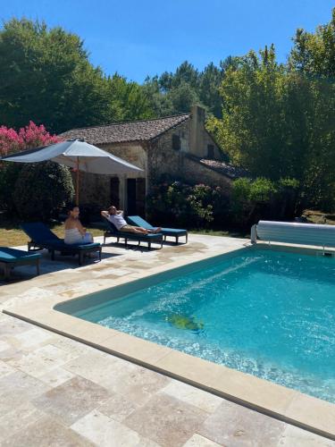 une piscine avec deux personnes assises sur des chaises et un parasol dans l'établissement Cottage avec piscine la clairière des secrètes, à Saint-Jean-dʼEstissac