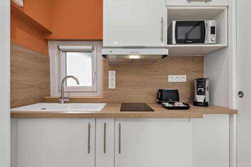 une cuisine avec des armoires blanches, un évier et un micro-ondes dans l'établissement Le cocon rouennais - Terrasse - Climatisation - Gare, à Rouen