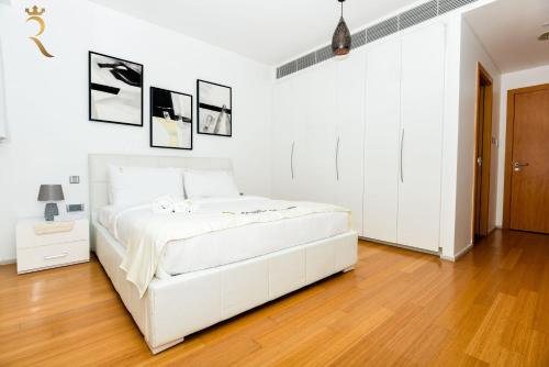 a white bedroom with a white bed and a wooden floor at 2BR Stylish Escape - Mariana Luxe Al Raha in Abu Dhabi