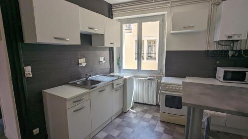 une cuisine avec des armoires blanches, un évier et une fenêtre dans l'établissement appartement rénové-équipé en centre-ville, au Puy-en-Velay
