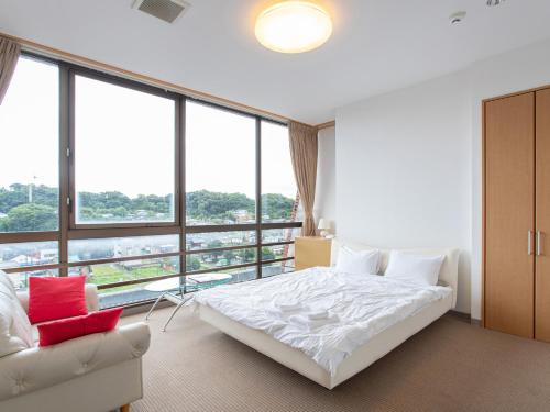 a bedroom with a white bed and a large window at Tabist New World Hotel Kagoshima Kanoya in Kanoya