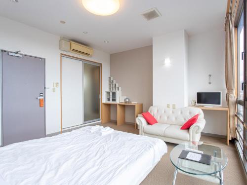 a bedroom with a white bed and a couch at Tabist New World Hotel Kagoshima Kanoya in Kanoya