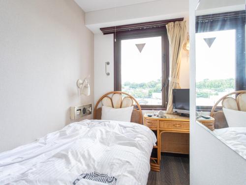a bedroom with a bed and a desk with a television at Tabist New World Hotel Kagoshima Kanoya in Kanoya
