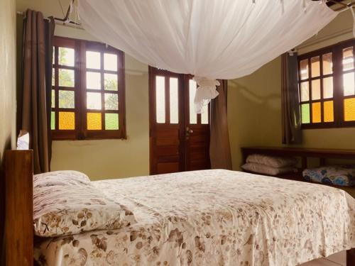 a bedroom with a bed with a white comforter and windows at Chalé Jaqueira in Palmeiras
