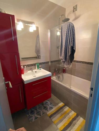 La salle de bains est pourvue d'une armoire rouge, d'un lavabo et d'une baignoire. dans l'établissement Appartement T2 entier et spacieux près du centre historique de Bayonne, à Bayonne