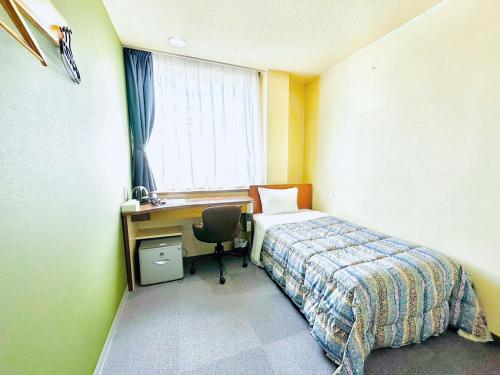 a bedroom with a bed and a desk and a window at Station Business Hotel Tenshukaku in Hitoyoshi