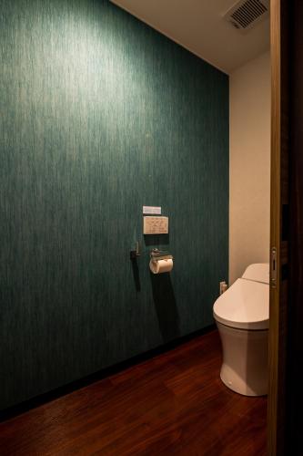a bathroom with a toilet and a green wall at The Peridot Smart Hotel Tancha Ward in Onna