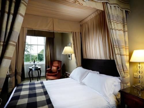 a bedroom with a bed and a chair and a window at Macdonald Linden Hall Hotel, Golf & Spa in Longhorsley