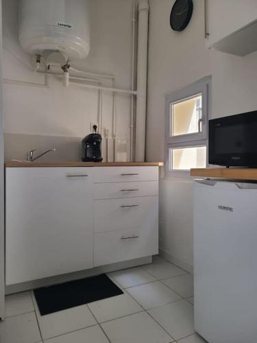 Il comprend une cuisine avec des placards blancs, une télévision et une fenêtre. dans l'établissement Appartement Cosy et Calme - Centre historique, à Montpellier