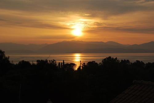a sunset over the water with mountains in the background at Penelope Apartment Hotel in Dassia