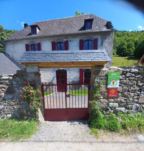 a house with a red gate and a stone wall at Gîte Chez Arnaoutou in Beaudéan