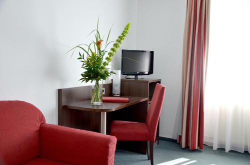 Habitación con escritorio, TV y jarrón de flores. en Hotel Am Römerwall en Mainz