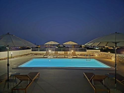 una piscina con sillas y sombrillas por la noche en Kalimera House, en Marina di Noto