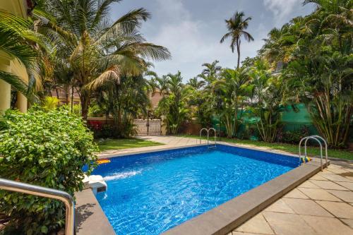 a swimming pool in a yard with palm trees at De Mandarin Beach Resort Suites & Villas, Candolim in Candolim