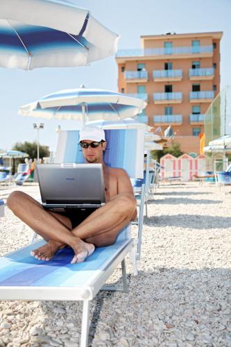 a man sitting on a beach chair with a laptop at Abbazia Club Hotel Marotta in Marotta