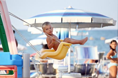 a baby sitting in a swing at the beach at Abbazia Club Hotel Marotta in Marotta