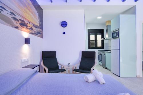 a bedroom with two chairs and a bed and a kitchen at Apartamentos Bellamar in Barbate