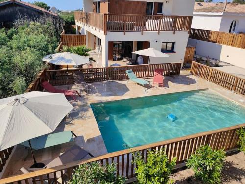 une piscine avec des parasols et des chaises ainsi qu'une maison dans l'établissement Villa Rose jacuzzi vue mer, à Lacanau
