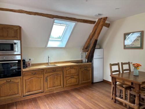 une cuisine avec des armoires en bois, une table et une fenêtre dans l'établissement Moulin Les Riaux, à Châtillon-sur-Indre