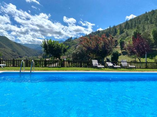 a blue swimming pool with two chairs and mountains at Apartamentos Calm & Nature - Adults Only in Cabezón de Liébana