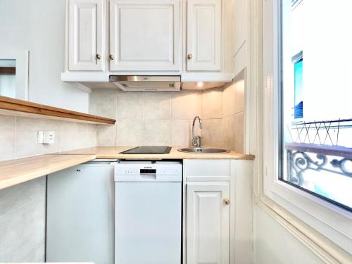 une cuisine avec des armoires blanches, un évier et une fenêtre dans l'établissement Appartement - Paris 16 - Passy, à Paris
