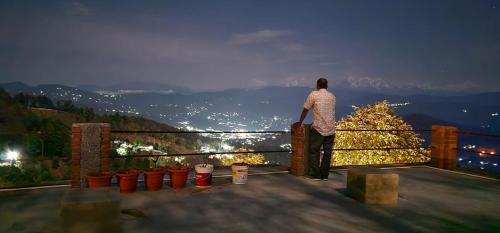 a man standing on a balcony looking at the city at Golden Himalaya Homestay in Kausani