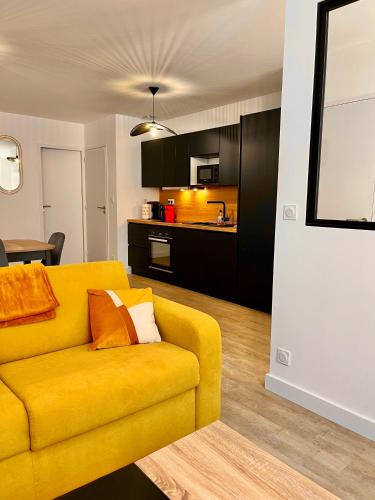 un salon avec un canapé jaune et une cuisine dans l'établissement T2 Rez-de-chaussée, Le Victor Hugo, à Cancale