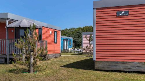 a red building next to a house with a tree at Molecaten Park Noordduinen in Katwijk