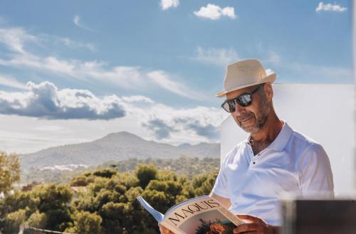 a man in a hat is reading a book at Hôtel Liberata & Spa in LʼÎle-Rousse