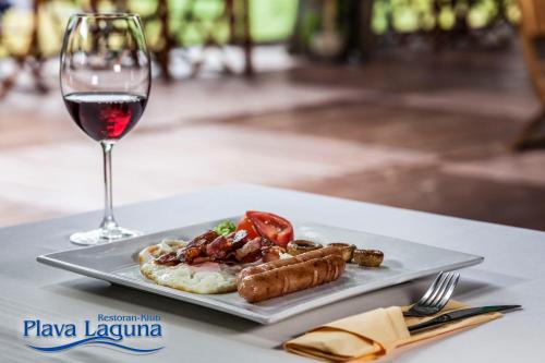 a plate of food and a glass of wine on a table at Garni Hotel Plava Laguna in Ćuprija