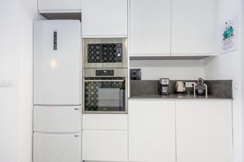 a white kitchen with white cabinets and an oven at Artisan Haven: El Cabanyal Oasis in Valencia