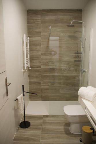 a bathroom with a toilet and a glass shower at Apartamentos Los Miliarios in Carcaboso