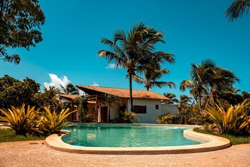 a pool in front of a house with palm trees at Paka Bangalos, Pousada de Charme em Sergipe in Pacatuba