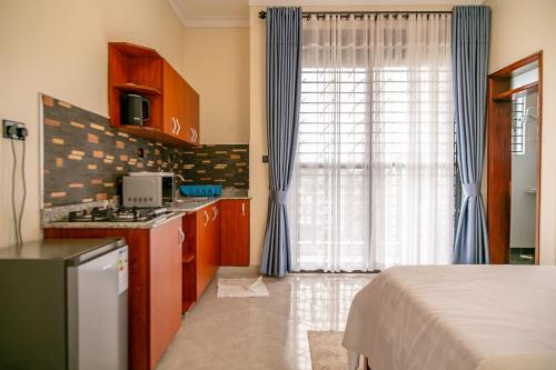 a room with a bed and a kitchen with blue curtains at iKHAYA RESIDENCES MUNYONYO in Kampala