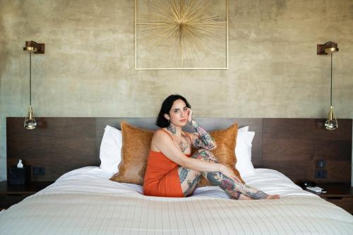 a woman with tattoos sitting on a bed at Bajo Estrellas Hotel Contemporáneo in Valle de Guadalupe
