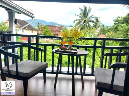 a table with two glasses and two chairs on a balcony at Meunna Boutique Hotel in Luang Prabang