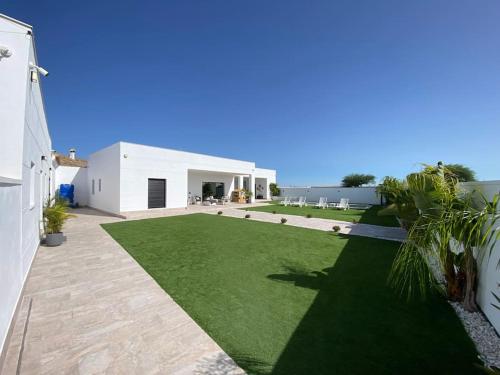 a backyard with a lawn and a white house at Villa con piscina Camino Doñana in Sanlúcar de Barrameda