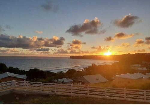 a sunset over the ocean with a white fence at Les Tourterelles - Appartement vue mer & jacuzzi in Le Lorrain