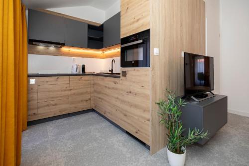 a kitchen with wooden cabinets and a tv and a plant at ALURE RESIDENCES 11 - 24h self check-in & private parking next to the apartment building included, CITY CENTER right on SNP Square in a quiet passage, new building, best deal in town in Banská Bystrica