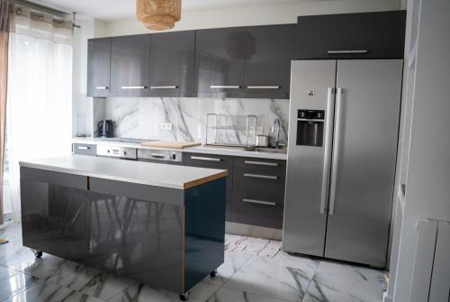 une cuisine avec des armoires noires et un réfrigérateur en acier inoxydable dans l'établissement Appartement 4 chambres proche Stade de France, parking et balcon sur jardin, à Aubervilliers