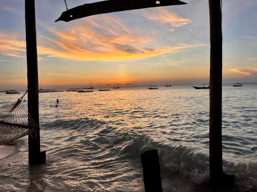 a sunset over the ocean with boats in the water at BamBam Bungalows Zanzibar in Nungwi