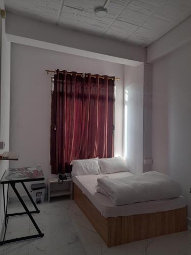 a bedroom with a bed and a window with a red curtain at THE LUSHAI INN in Āīzawl