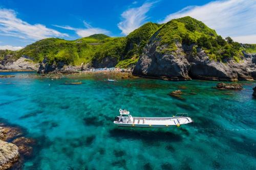 a boat in the water next to a mountain at 和みの宿 弓ヶ浜いち番館 in Minamiizu